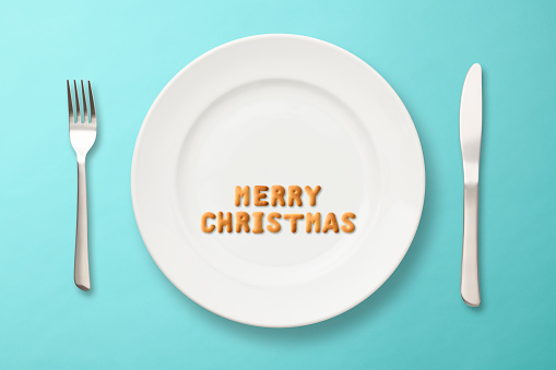 MERRY CHRISTMAS written with biscuits on a white plate with copy space, on light blue background.
With Knife and Fork