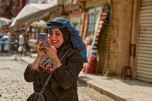 cairo, Egypt – October 27, 2023: An Arabic woman wearing a traditional headscarf while using her smartphone on a street in Cairo, Egypt.