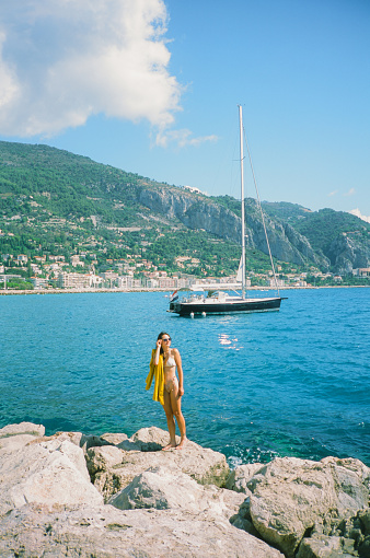 A woman with sunglasses and with  yellow beach towel standing near the yacht on the French riviera