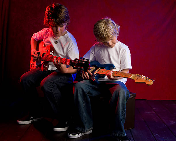 Older brother teaches younger brother to play guitar on the makeshift stage in their garage.