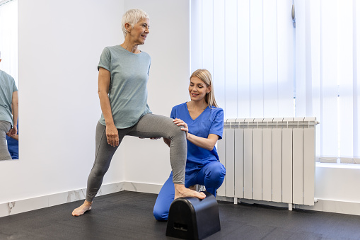 Senior patient at the physiotherapy doing physical exercises with her therapist, doing leg physiotherapy for elderly woman, to treat osteoarthritis and nerve pain in the leg.