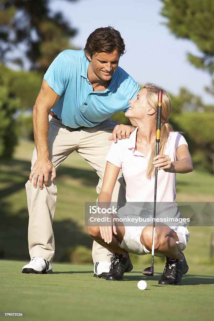 Couple Golfing On Golf Course Lining Up Couple Golfing On Golf Course Lining Up On Putting Green Looking At Each Other Chatting 20-29 Years Stock Photo