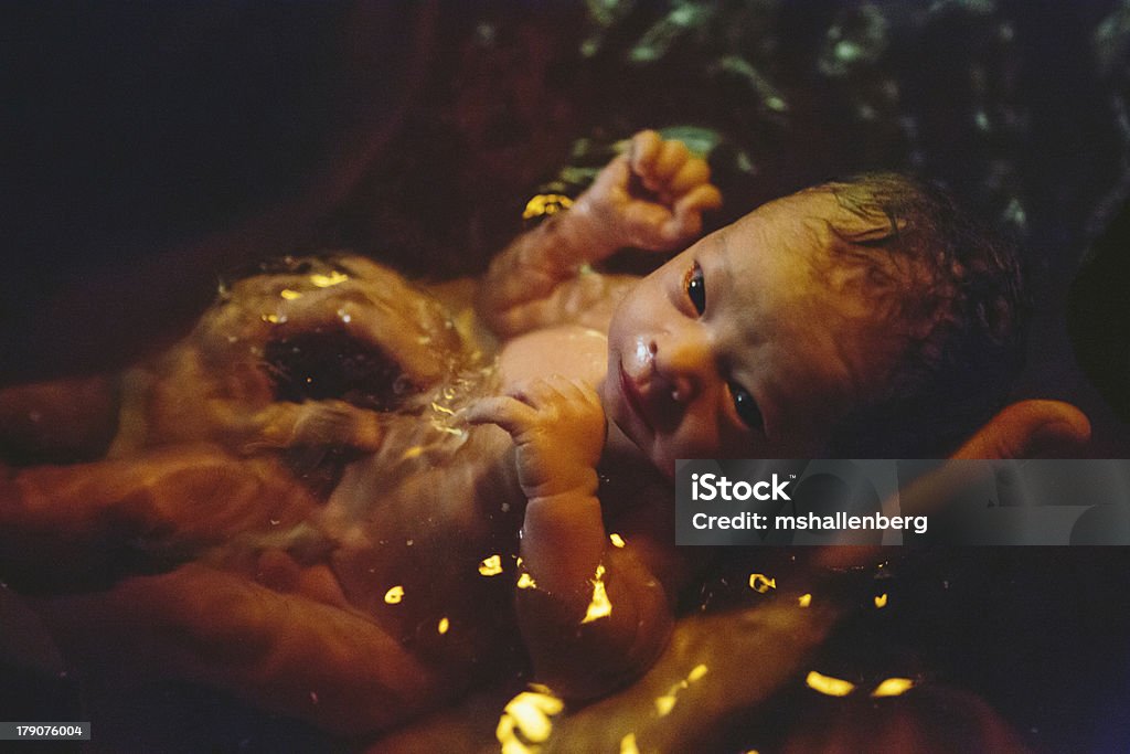 Newborn soaking in birthing pool "A newborn baby, with umbilical cord still attached, soaks in the water of the birthing pool, eyes gazing up at it's mother. Lowlight, late night home birth with midwives." Water Birth Stock Photo