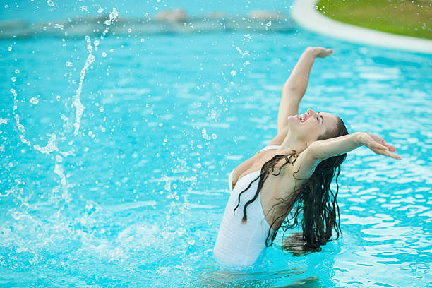 istock Happy young woman splashing water in pool 179076942