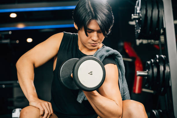 istock handsome young Asian man sitting on an exercise bench holding a heavy dumbbell 1790770379