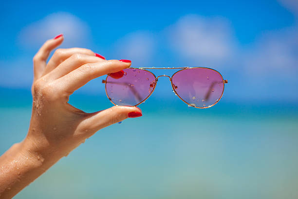 Woman's hands holding pink sunglasses on tropical beach Woman's hands holding pink sunglasses on tropical beach tinted sunglasses stock pictures, royalty-free photos & images