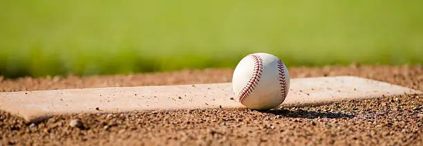 a leather baseball lying next to the pitching rubber on a pitching mound