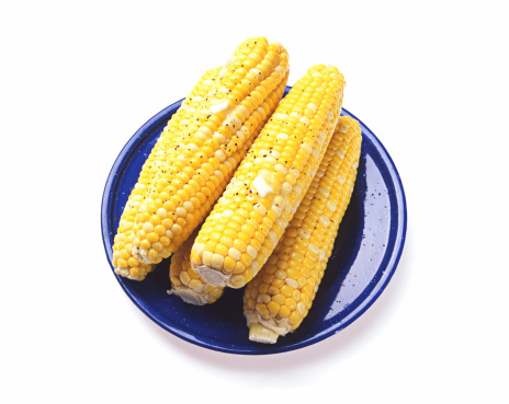Yellow corn on a blue plate, with melted butter. White background. Digitally captured from film source.
