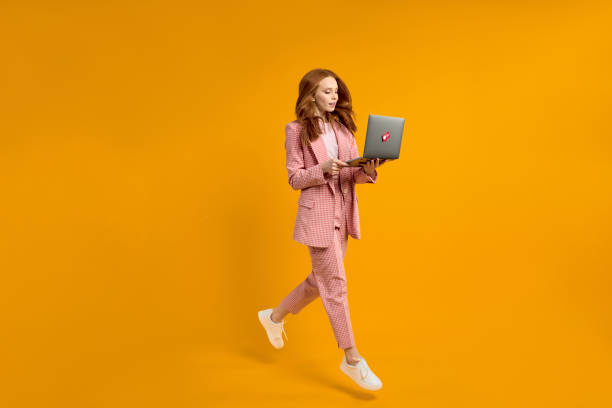 Happy jumping woman with laptop isolated on yellow background. Modern technologies