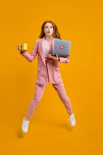 zmartwiona liderka skacze w powietrzu niosąc laptopa i kawę biegnącą szybko się spieszy - vertical studio shot indoors pink zdjęcia i obrazy z banku zdjęć