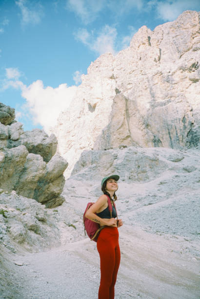 Cheerful woman with backpack wearing cap  hiking in Dolomites. Shot on camera film