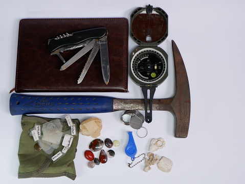 Geological fieldwork tools such as Brunton Compass, geology hammer, pocket knife, magnifying glass with some minerals chalcedony and calcite