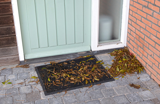 Green and brown autumn leaves piling up in front of the doorstep of a wooden door