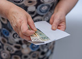 An elderly woman puts money, Polish banknotes, into an envelope