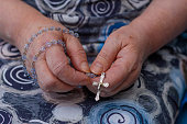 An elderly woman holds a rosary with a cross in her hands and prays to God