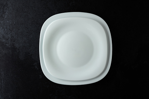 Empty white plates on a black stone table. Top view, copy space.