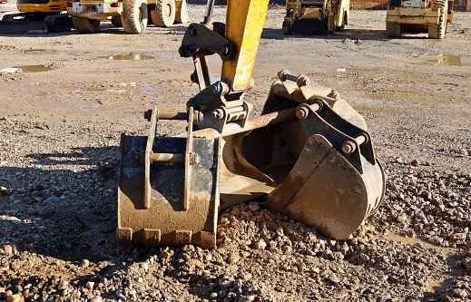 Group of different bucket types under the excavator boom on the dirt of a construction site. Construcion machineries on background.