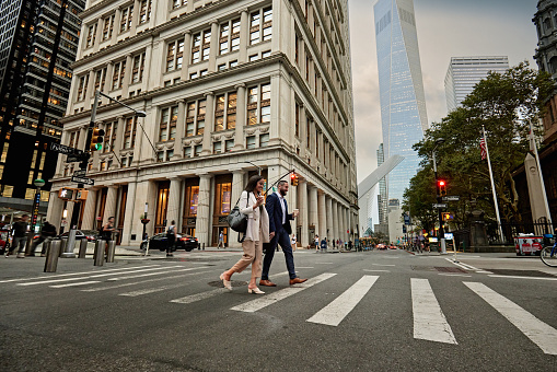 Full length view of colleagues in 20s and 30s crossing Fulton Street in Lower Manhattan, One World Trade Center in background.