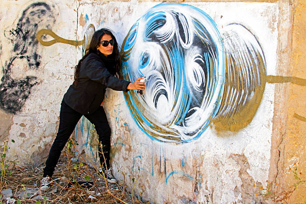 istock Woman in black spraying at a graffiti brick wall 179086276