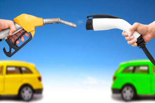 electric car and gasoline car concept. hand holding gas pump and power connector for refuel