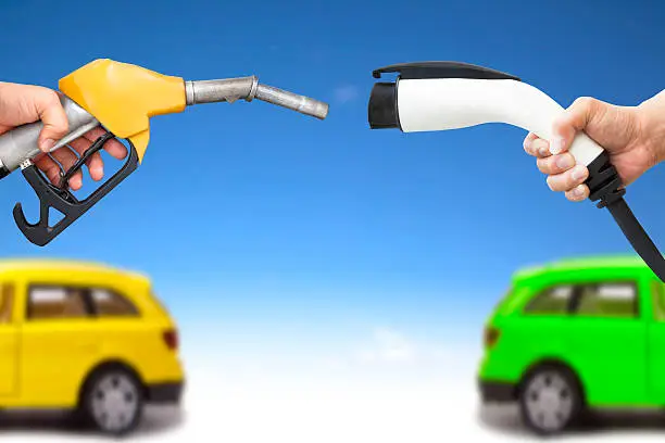 electric car and gasoline car concept. hand holding gas pump and power connector for refuel