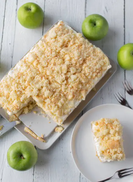 Delicious homemade apple cream cake with green apples. Served whole and sliced on white wooden background from above. Baking recipe, ideas or concepts for social media