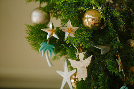 Closeup of decorations hanging on Christmas tree. Vintage wooden ornaments: stars, angels and colorful baubles