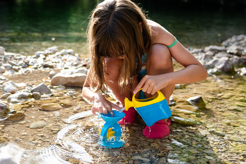 Full length of a girl plays with plastic buckets in the river at summer day