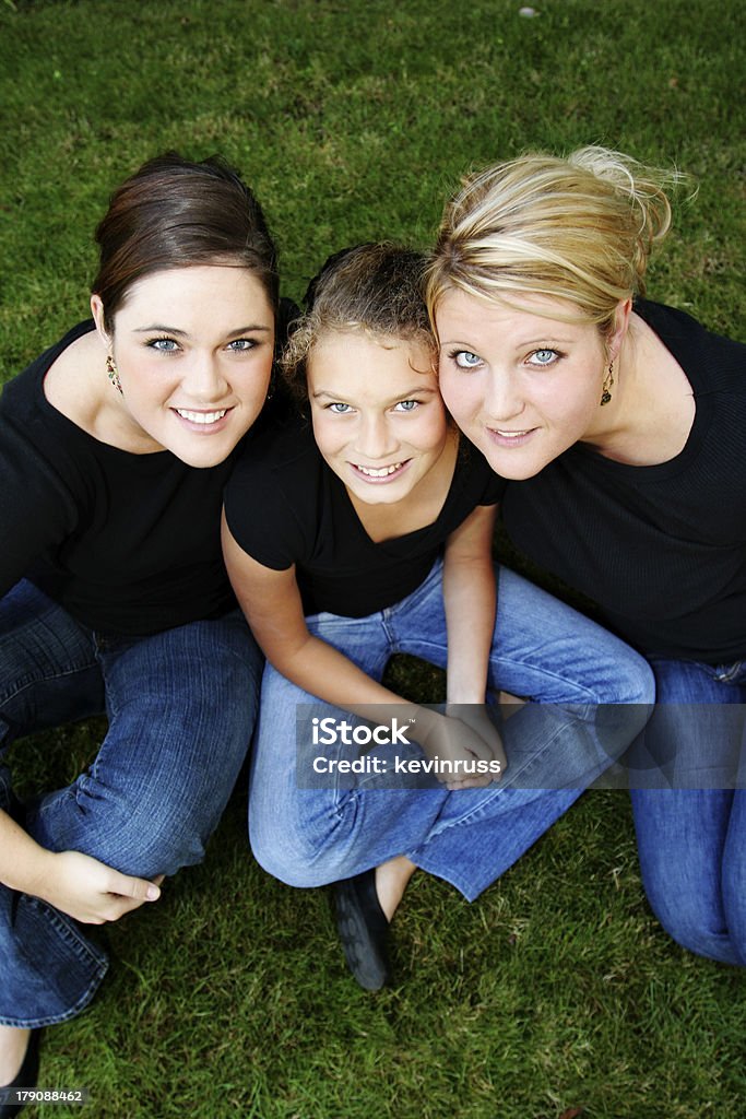 Tre sorelle seduto nell'erba - Foto stock royalty-free di Abbigliamento casual