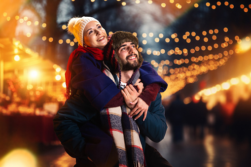 Happy couple smiling happiness standing and hugging outdoors on winter fair before Christmas. Spend time together. Concept of national traditions, winter holidays, fashion, festivities