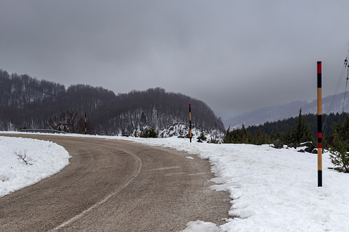 Winter in the mountains. Pine forest in the highlands (Epirus region, Greece) and country road on a winter, cold and snowy day