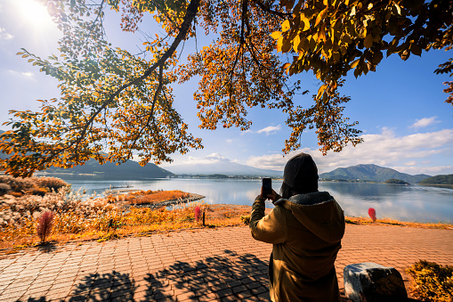 Asian woman travel alone in Japan at Lake Kawaguchiko in autumn with Mount Fuji view.