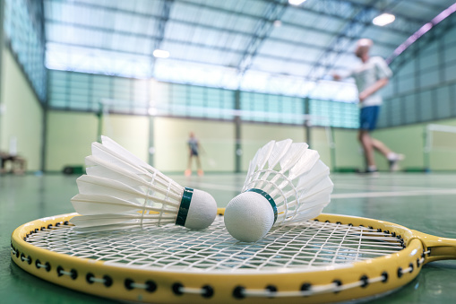Close up shuttlecock on badminton racket at courts with players competing