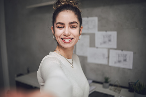 Selfie of a young beautiful woman taking a picture in her apartment, wearing a cream blouse, picture for social media or AI apps on mobile phone