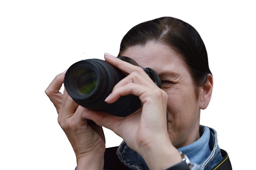 Professional photographer - woman in the process of shooting. Portrait of a Caucasian brunette woman in a denim jacket holding a camera, isolated on a white background.