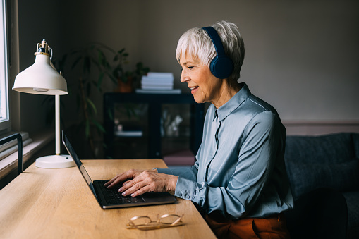A focused senior Caucasian woman delves into her work, donning a pair of headphones that transport her into a realm of concentration.