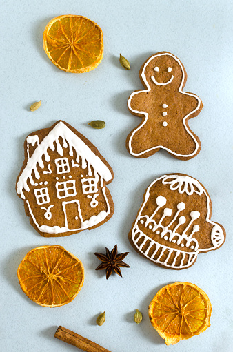 Gingerbread cookies with white frosting and dried orange slices and spices on a gray background. Baking in the form of a man, a house and gloves. The concept of festive food. Vertical orientation