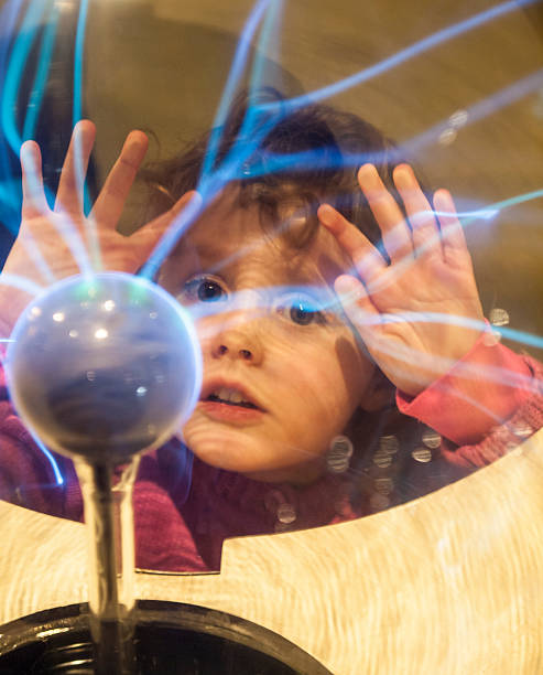 small girl touches a plasma ball with her hands and watches the electrostatic discharge