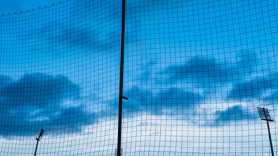 Football pitch fencing in the form of a protective net. Ball catcher. Silhouette of stadium spotlights against the blue sky. Blue hour