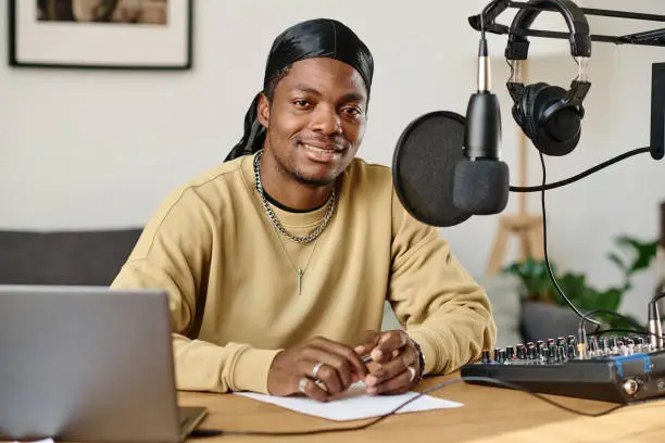 Photo of Guy sitting by workplace with microphone, headphones, soundboard and laptop