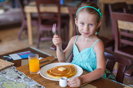Little girl having breakfast with juice and pancake at resort restaurant