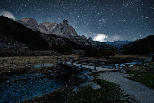 French alps landscape of starry night sky over Claree valley with Main De Crepin peak and river flowing during autumn at Hautes Alpes, France