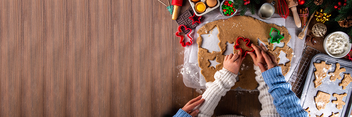 Cooking Christmas cookies family background. Mother and daughter hands top view on cozy wooden background, making gingerbread biscuits with cookie cutters, with New Year Christmas decoration