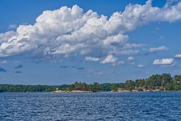 A tranquil lake surrounded by lush greenery, illuminated by a bright blue sky dotted with white clouds