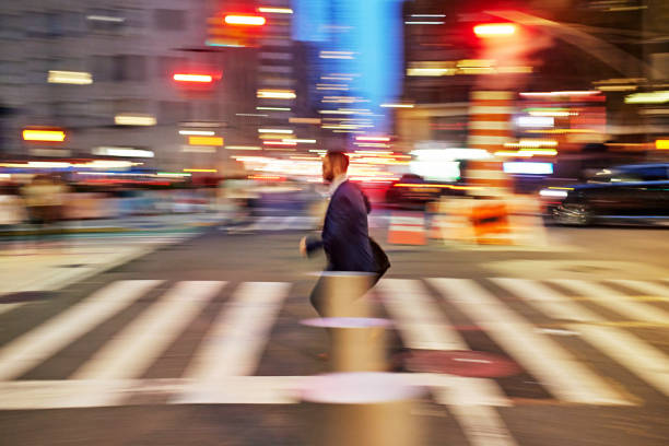 Full length side view of mid adult professional in office attire running across illuminated street after work, traffic and twilight sky in background.