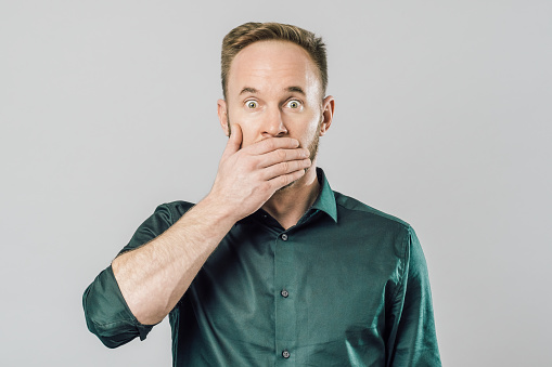 Close up of funny handsome young man with in stylish green shirt looking in camera with surprised face expression. Isolated on gray