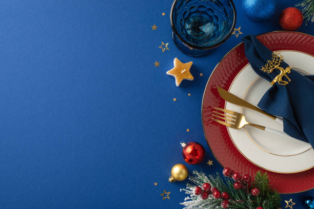 istock Impeccable Christmas table arrangement with plates, gilded utensils, napkin, crystal goblet, glittering baubles, radiant star candle, confetti, hoarfrost-covered fir twigs, berries on blue canvas 1791029863