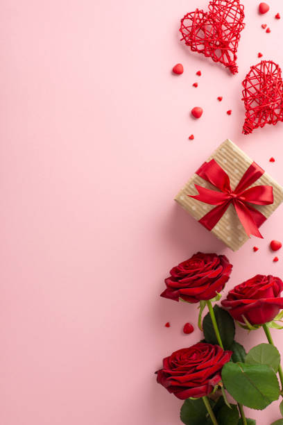 istock Set the scene for Valentine's Day with vertical top view rustic gift box, heart-shaped rattan decor, red roses, sugar sprinkles on a pastel pink backgroundâready for your text or ad 1791029864