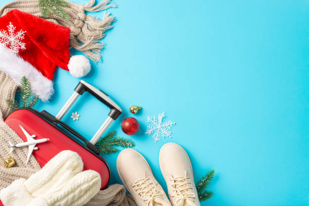 istock Festive Flight: Overhead composition featuring a red suitcase, miniature airplane, Santa's attire, baubles, jingle bell and wintery details against a bright blue backdrop for your festive messages 1791029875