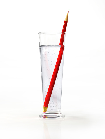Tall glass of water, with a red pencil inside. On white surface and background.